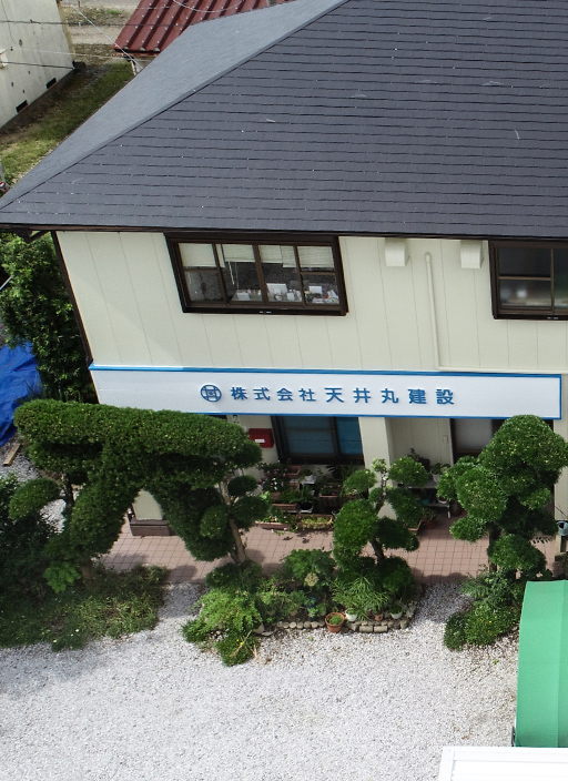 株式会社天井丸建設の看板が掲げられた2階建てオフィス外観。手入れの行き届いたトピアリーの庭と砂利敷きの玄関先